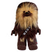 A plush toy resembling Chewbacca from Star Wars. The Little Shop of Magic LEGO Star Wars: Chewbacca Plush Minifigure has long brown fur with tan highlights on the face and chest. It is wearing a brown bandolier with gray squares across the chest and has paw-like hands and feet, with flames on the legs. The toy has a friendly expression, perfect for soft toy play or recreating Star Wars scenes.