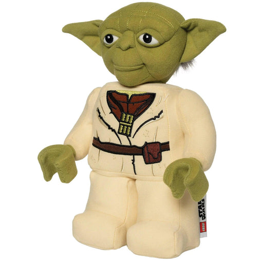 A LEGO Star Wars: Yoda Plush Minifigure from Little Shop of Magic. The toy has large green ears, green skin, and wide eyes. It is wearing a beige Jedi robe with a brown belt printed on the fabric. The tag on the toy's side features the Star Wars logo. The toy has a soft, stuffed appearance.