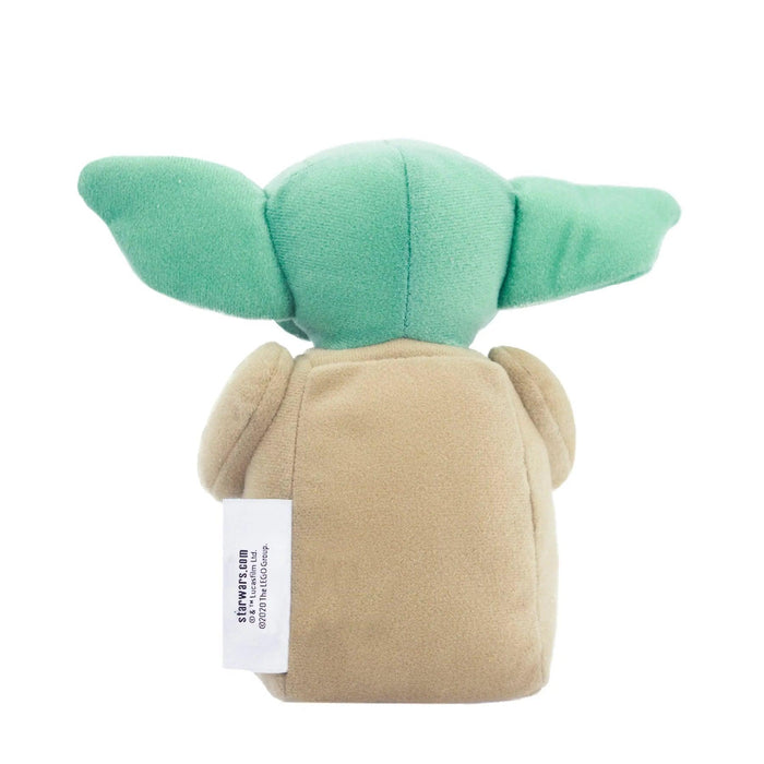 A LEGO Star Wars: The Child Plush Minifigure from *Little Shop of Magic*, featuring large green ears and a green head. The body is beige with a visible white tag on the left side, containing manufacturing details. The toy has a soft, cuddly texture and a rounded shape.