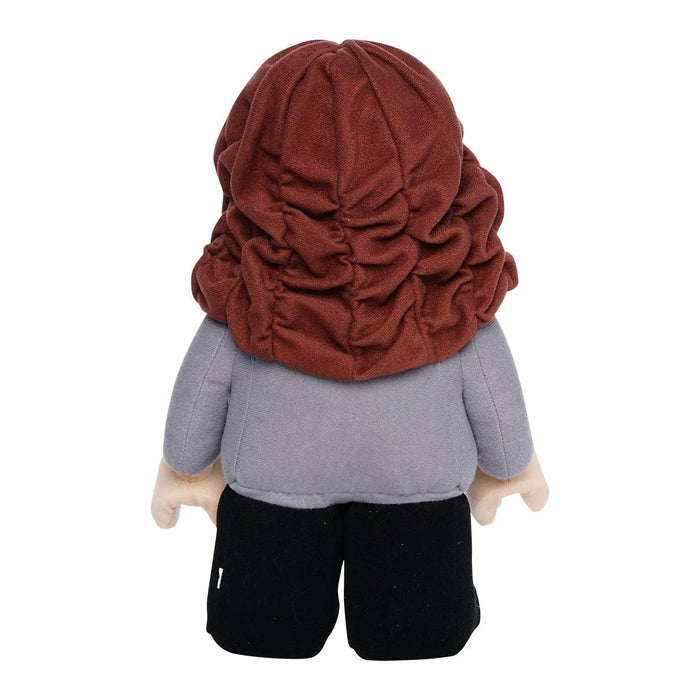 A LEGO Harry Potter: Hermione Granger Plush Minifigure with long, tousled brown hair viewed from the back, reminiscent of Little Shop of Magic. The toy is dressed in a gray top and black pants, and has light beige hands and feet. The facial features are not visible due to the toy facing away.