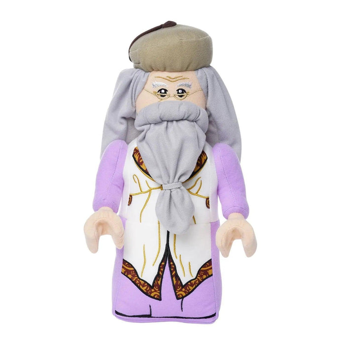 A Little Shop of Magic LEGO Harry Potter: Albus Dumbledore Plush Minifigure designed to resemble a historical figure. The toy has a gray beard, long gray hair, and wears a beige cap. It is dressed in a purple robe with a detailed white apron featuring brown patterns. Inspired by the Harry Potter books, it has simple, minimalistic facial features and beige hands.