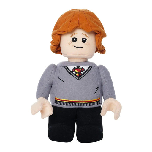 A Little Shop of Magic LEGO Harry Potter: Ron Weasley Plush Minifigure depicts a character with orange hair, freckles, and a smiling face. Wearing a grey sweater with a red and yellow striped tie underneath, black pants, and black shoes, this Harry Potter figure has a friendly and approachable appearance with soft, rounded features.