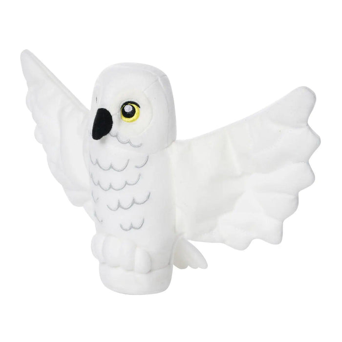 A Little Shop of Magic LEGO Harry Potter: Hedwig the Owl Plush Minifigure resembling a white owl with outstretched wings. The owl has black and grey detailing for beak and feathers, and vivid yellow eyes with black pupils. Reminiscent of a LEGO Hedwig plush, the toy is standing upright, showcasing its soft texture and wing span in a simplistic, cartoonish design.