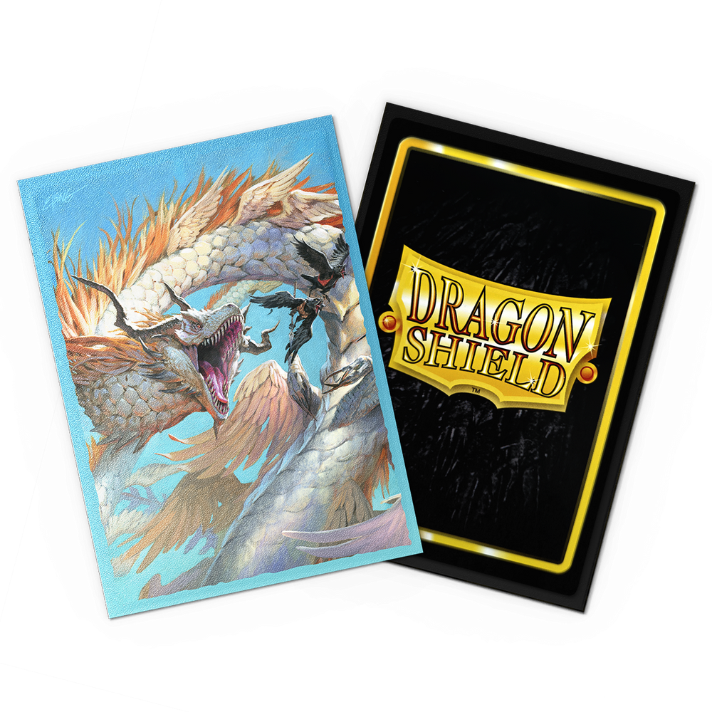 A vibrant card on the left showcases an ice dragon with icy blue scales and fierce eyes, breathing frost. On the right, another card features the Arcane Tinmen "Dragon Shield" logo on a reflective black and gold background, hinting at their protective trading sleeves. Both are slightly tilted.