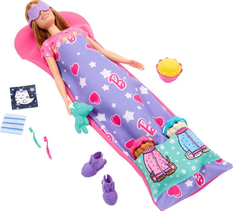 A Mattel Barbie-Slumber Party Puppies-Doll Set features a doll lying on a pink mat, covered in a purple blanket with heart and celestial designs. She wears an eye mask and holds a teddy bear. Accessories include two slippers, a kitten picture, a flower-shaped bowl, a toothbrush with toothpaste, and two dog-themed socks.