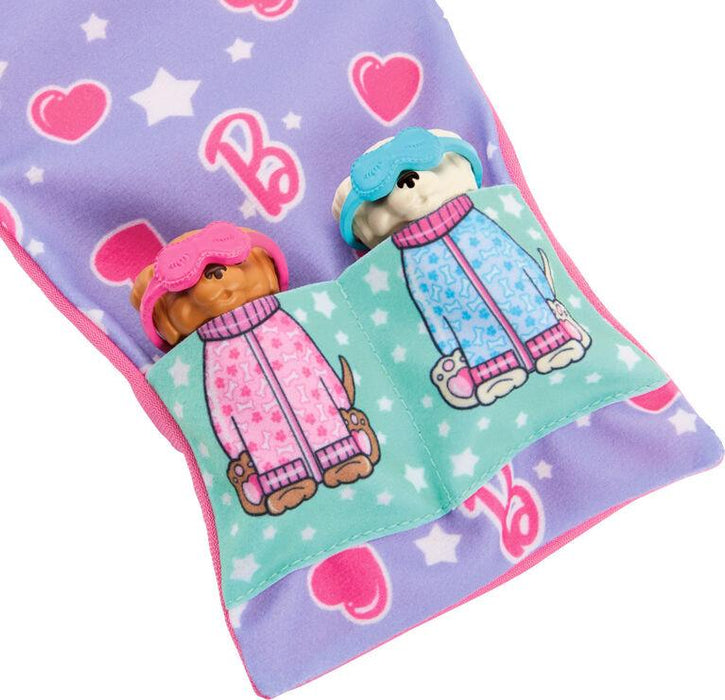 Two small toy dogs in a soft, pastel purple sleeping bag. Each dog is tucked into its own pocket—one teal, the other light green. Wearing pink and blue pajamas with eye masks, the dogs look like they're part of a Barbie-Slumber Party Puppies-Doll Set. The sleeping bag features hearts, stars, and the letter "B," from Mattel.