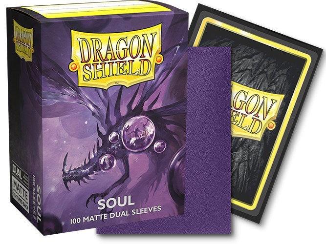 A box of Arcane Tinmen Dragon Shield: Standard 100ct Sleeves - Soul (Dual Matte) is depicted. The box features a dragon with orbs on a purple background. Next to the box are a single metallic purple sleeve and the black backside of another sleeve. The Dragon Shield logo is prominently displayed on the box and the sleeve.