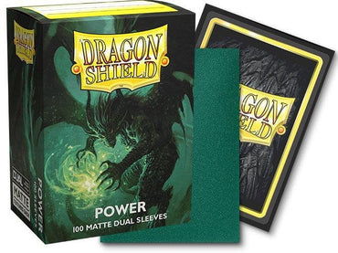 The image shows a box of Arcane Tinmen Dragon Shield: Standard 100ct Sleeves - Power (Dual Matte) labeled "Power," specifically 100 matte dual sleeves. The box features artwork of a green dragon surrounded by mist. In front of the box are a single green trading card sleeve and the back of a sleeved card.