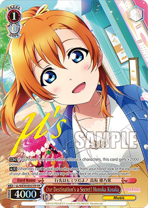 A colorful trading card from Bushiroad features an anime girl with orange hair and blue eyes, wearing a white shirt with a pink tie and a blue jacket. She looks surprised, with a decorated flower pot and blurred background behind her. This Love Live! School Idol Festival 10th Anniversary card is named "Our Destination's a Secret! Honoka Kosaka (LL/WE39-E031FP FP).