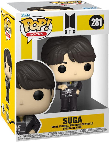 The image shows a Funko Pop! Rocks BTS - Suga vinyl figure from Funko in its packaging. The mostly white and yellow box features a clear plastic window displaying the figure. Numbered 281, Suga is dressed in a dark outfit with a detailed expression and hairstyle, making it a must-have for BTS fans.