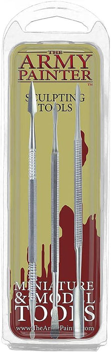 A clear plastic packaging containing three metal sculpting tools labeled "The Army Painter Clay Sculpting Tools." The tools, ideal for Green Stuff carving, feature different small, precise tips for miniature and model detailing. The background of the packaging is yellow and red with text and silhouetted figurine graphics.