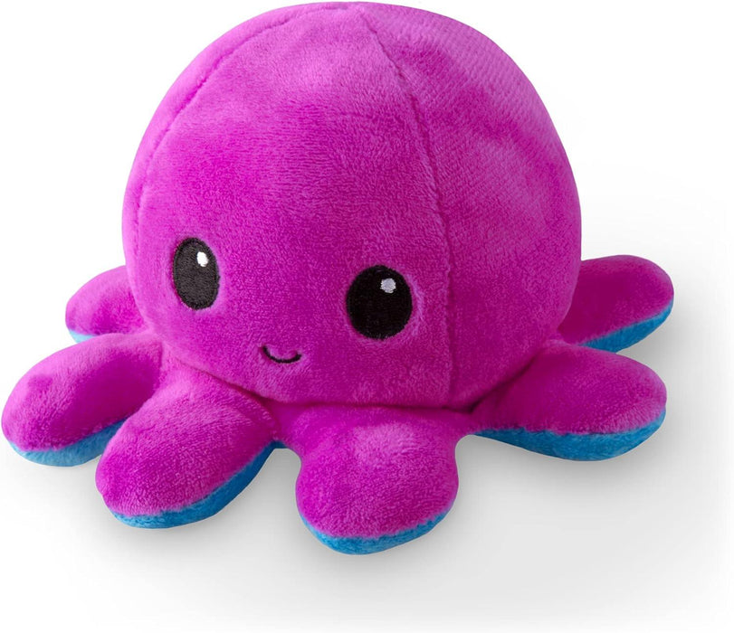 A TeeTurtle Reversible Blue and Purple Octopus Plushie, featuring a bright pink body with eight short tentacles. The lower parts of the tentacles are blue. It has large, round, black eyes with white highlights and a small, smiling mouth. This reversible octopus plushie is part of our collection of super soft toys from Everything Games and boasts a fuzzy texture.