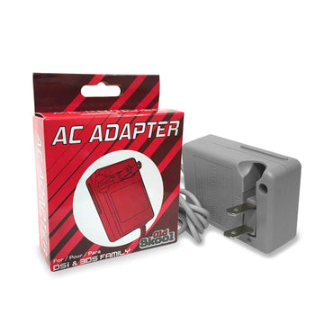 A red and white Old Skool box labeled "DSi & 3DS System AC Power Adapter" sits beside a gray, high-quality AC adapter with a two-prong plug, indicating compatibility with DSi and 3DS devices. A coiled charging cable is attached to the adapter.