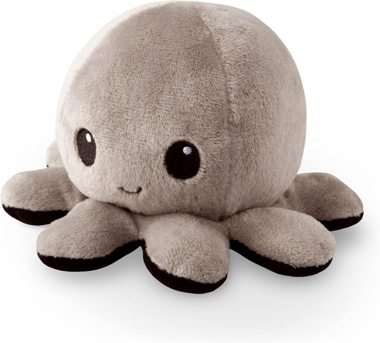 A **TeeTurtle Reversible Black and Gray Octopus Plushie** by **Everything Games**, with a round, fluffy body and eight short, stubby legs. It features dark tips on its legs and two large, round, black eyes with small white reflections alongside a small, curved smile embroidered on its face. This trending TikTok toy is set against a white background.