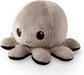 A **TeeTurtle Reversible Black and Gray Octopus Plushie** by **Everything Games**, with a round, fluffy body and eight short, stubby legs. It features dark tips on its legs and two large, round, black eyes with small white reflections alongside a small, curved smile embroidered on its face. This trending TikTok toy is set against a white background.