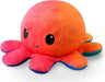 A round, plush toy shaped like an octopus, this TeeTurtle Reversible Sunset and Mermaid Octopus Plushie by Everything Games features a vibrant gradient of red to orange with a light blue edge along its legs. Large, black embroidered eyes and a small, smiling mouth give it a cute and cheerful appearance—making it the perfect gift.