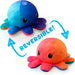 Two TeeTurtle Reversible Sunset and Mermaid Octopus Plushies by Everything Games are displayed. One is blue and dark blue with a sad expression, while the other is red and orange with a happy expression. Blue arrows indicate that the cute reversible plush octopuses can be flipped inside out to change their look. The word "REVERSIBLE!" is written in blue.