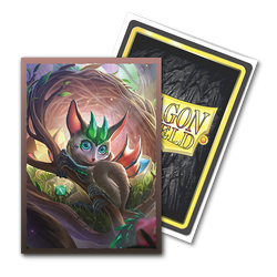 A fantasy trading card showcases a whimsical creature with large blue eyes, pointed ears, and a green leafy headdress, set against the backdrop of a vibrant forest with soft lighting. The textured back proudly displays "Dragon Shield" in yellow, as part of the Arcane Tinmen's TCG cards series. It's perfect for fans of Brushed Art sleeves and appropriately named "The Bushdrake.