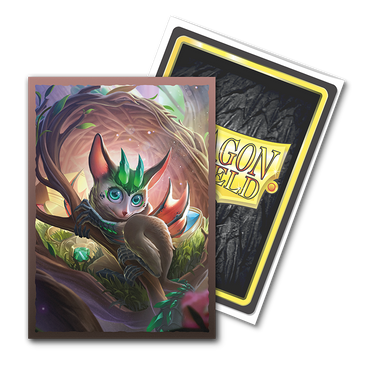 A fantasy trading card showcases a whimsical creature with large blue eyes, pointed ears, and a green leafy headdress, set against the backdrop of a vibrant forest with soft lighting. The textured back proudly displays "Dragon Shield" in yellow, as part of the Arcane Tinmen's TCG cards series. It's perfect for fans of Brushed Art sleeves and appropriately named "The Bushdrake.