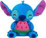 A Disney Stitch Feed Me Small Plush from Disney featuring a blue alien-like character with large purple inner ears and a small tuft of blue hair. Stitch is smiling with closed eyes and holding a slice of pink watermelon with black seeds and a green rind. This beanbag plush has a playful and adorable appearance.