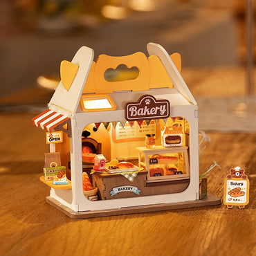 Teddy’s Breadbox by Robotime is a charming bakery model for table decor. It emits a warm glow, featuring a cozy counter with pastries and a cake, adorned with "Bakery" and "Open" signs. Its breadbox-shaped exterior showcases a striped awning on an elegant wooden base.