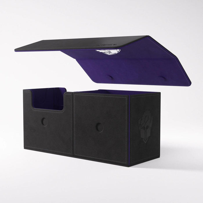 A black and purple premium deck box with an open lid. The innovative design features two compartments—one on the left with a shorter divider and one on the right with a taller divider. Lined with purple material, it boasts a crest or logo on the outer front side of the right compartment. Introducing THE ACADEMIC 133+ XL TOLARIAN EDITION - BLACK & PURPLE by Game Genic.