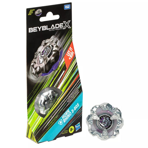 The image displays a boxed Hasbro Beyblade Horn Rhino Defense Battle Top Booster Pack toy. The packaging, featuring a predominantly black and green color scheme, prominently shows the Beyblade. The bottom right of the image features the unpackaged toy itself, highlighting its silver and purple design. Suitable for ages 8+.