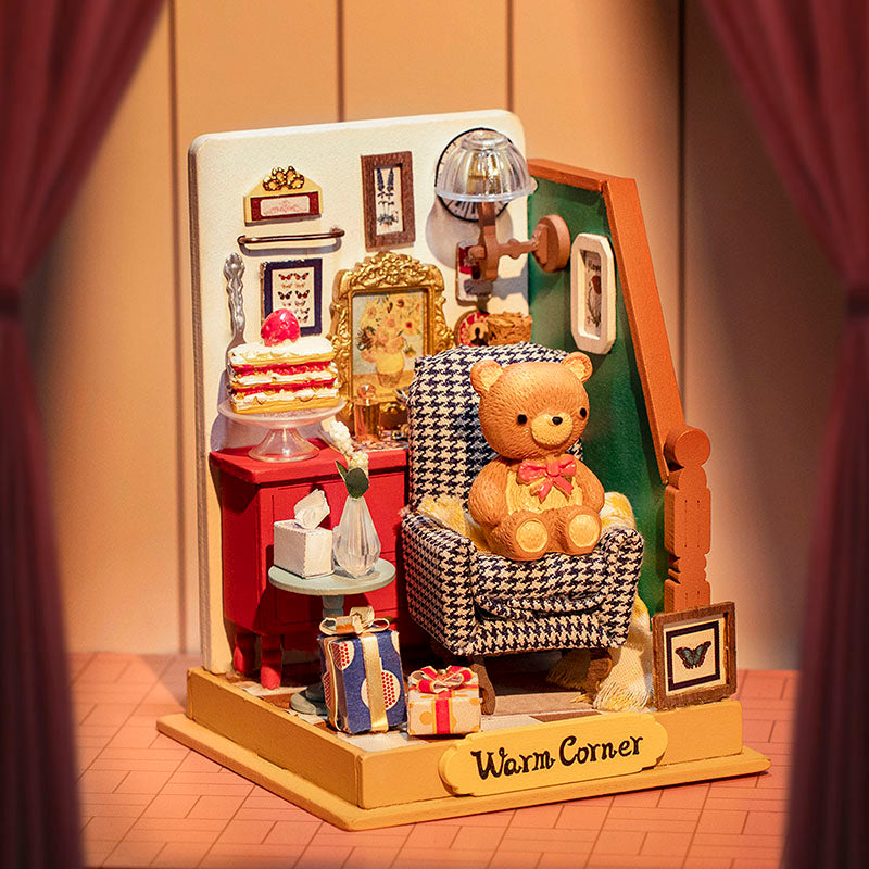 The Holiday Living Room by Robotime is a cozy, miniature setting featuring a plush teddy bear seated on a houndstooth armchair. Framed pictures, a red cabinet, a lamp, a cake, and neatly wrapped gifts surround the scene. This intimate space exudes warmth with its soft lighting and drawn curtains on the sides.