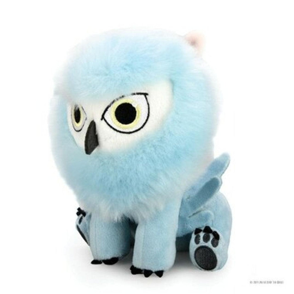 A KidRobot Dungeons & Dragons - Phunny Plush - Snowy Owlbear resembling a mythical creature with a large, round, light blue fluffy head, yellow eyes with black pupils, and a beak-like nose. It has blue wings and four blue limbs, each with black, paw-like detailing at the bottom. The toy is seated and facing forward.