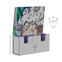 The SUN GOD EMBROIDERED DECK BOX by Dueling Guard is a grey vegan leather deck box adorned with an anime character illustration featuring a person with white, curly hair, visible teeth, and spiraled eyes. Its modular design includes three compartments for cards, and the interior showcases a striking purple hue. The "Dueling Guard" logo and name are prominently printed on the front.