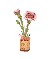A Rolife Rowood Pink Carnation 3D puzzle model of pink carnations in a kraft paper pot. The model features two blossoms in different stages of bloom, along with green leaves on intricately designed stems, all set in a beautifully decorated pot with a floral design.