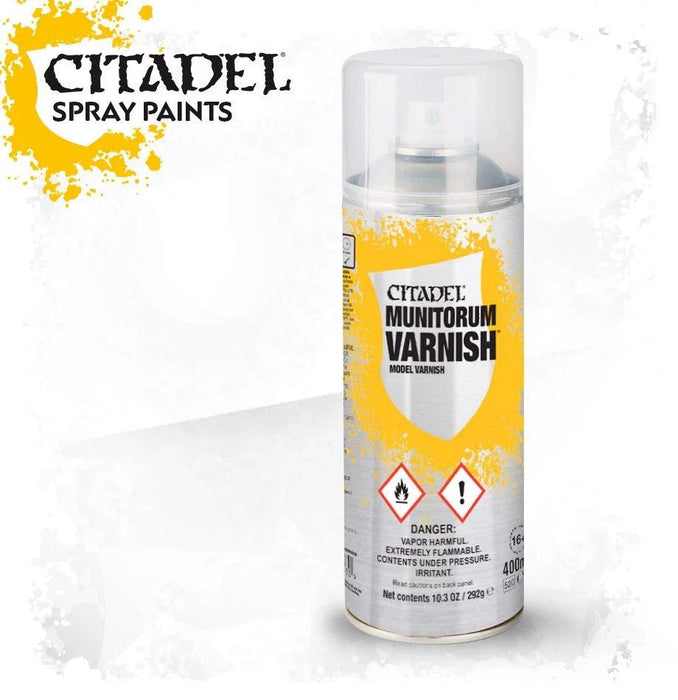 A cylindrical can of Citadel Colour - Munitorum Varnish is pictured against a white background with a paint splatter pattern. The label indicates it contains 400ml. Warning symbols for flammability and irritation are displayed on the front, along with usage directions and hazard information.