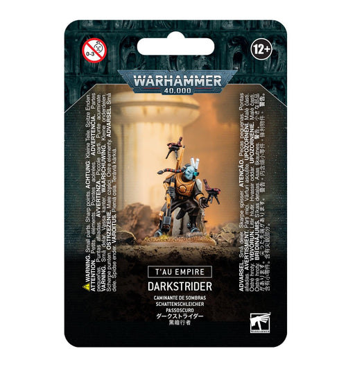 Packaging for the Games Workshop "T'AU EMPIRE: DARKSTRIDER" miniature kit, featuring an armored figure wielding a weapon amid sci-fi terrain. Background displays age 12+ warning and multilingual caution statements. The top has a "Warhammer 40,000" logo, and the bottom showcases the product name.
