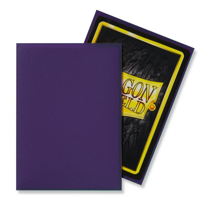 Two rectangular cards are displayed. The card on the left has a solid purple front. The card on the right is angled behind, showing its back, which has a black and yellow border with the text "AGOn ELd" partially visible against a dark background with texture. These cards are protected by durable Arcane Tinmen Dragon Shield: Standard 100ct Sleeves - Purple (Matte).