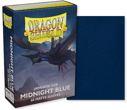 A box of Arcane Tinmen Dragon Shield: Japanese Size 60ct Sleeves - Midnight Blue (Matte), perfect for TCGs, is displayed. The box features an illustration of a black dragon flying against a stormy, mountainous backdrop. Beside the box, one of the 60 included dark blue Dragon Shield sleeves is shown.