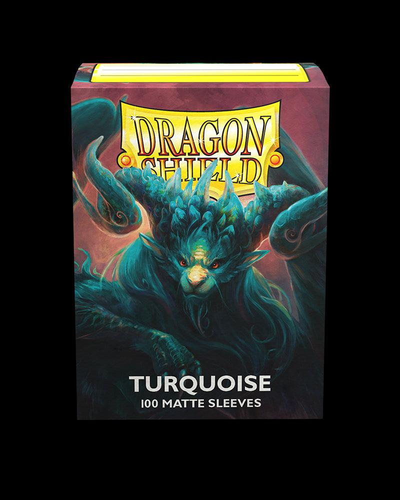 The image shows a box of Arcane Tinmen Dragon Shield: Standard 100ct Sleeves - Turquoise (Matte) for cards. The box features a vivid illustration of a menacing, mythical dragon-like creature with blue-green hues and intricate detailing, set against a dark red background. Perfect TCG accessories, the text reads 