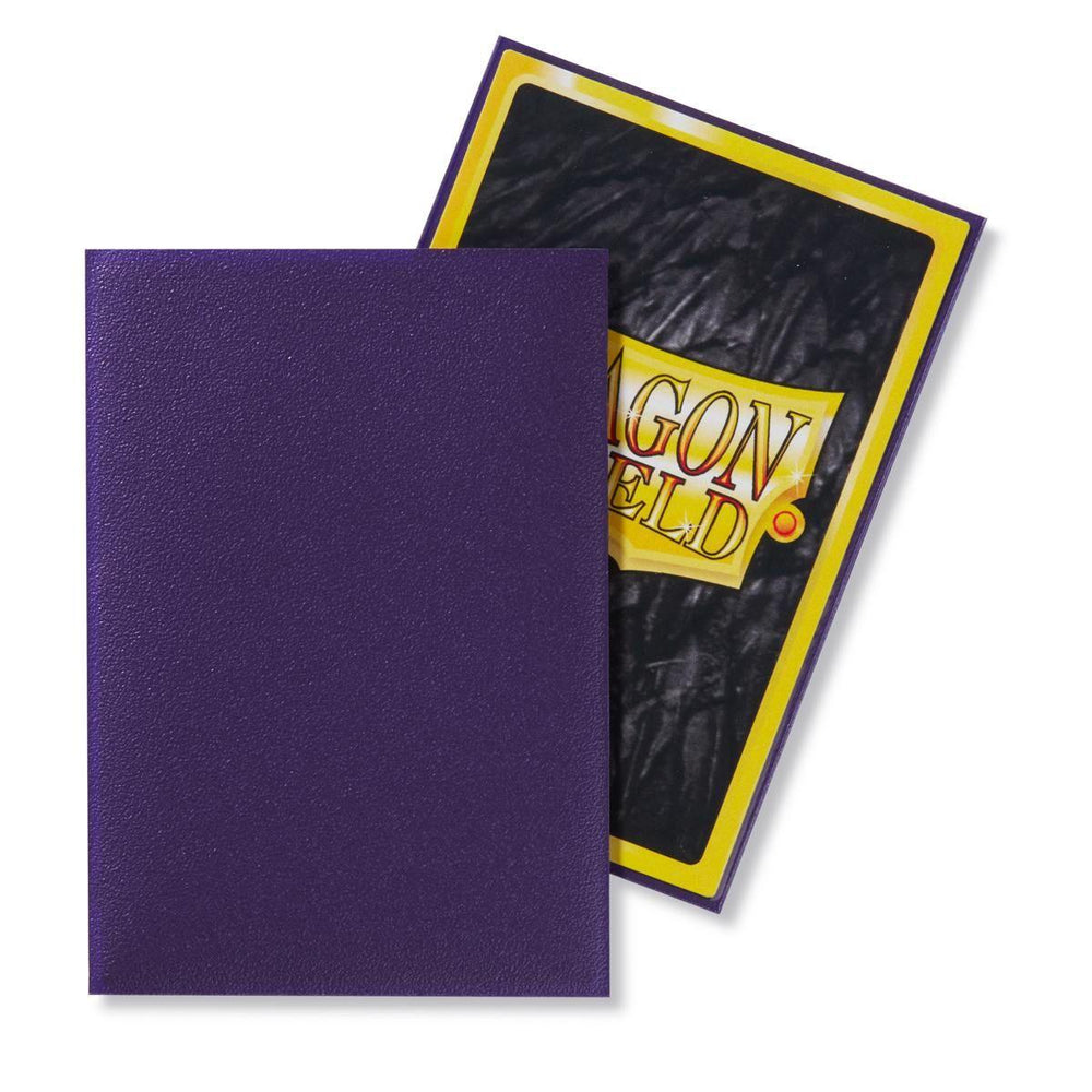 A textured purple card sleeve from the Dragon Shield: Japanese Size 60ct Sleeves - Purple (Matte) by Arcane Tinmen is displayed next to its packaging. The packaging features a design with a yellow border and a black background, prominently showcasing the text "Dragon Shield" in yellow with red details. These Japanese size sleeves provide both style and protection.