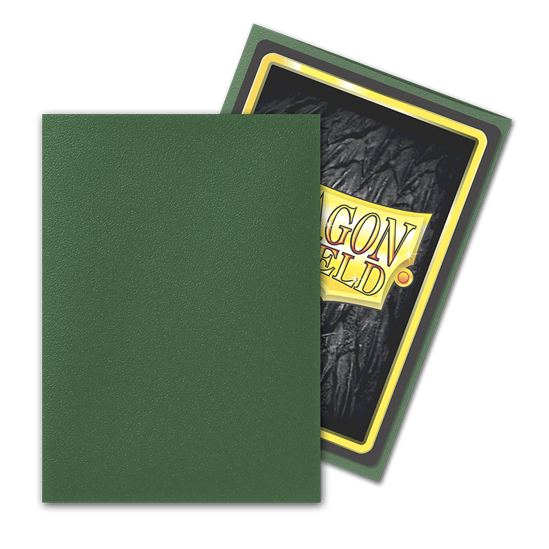 A Dragon Shield: Standard 100ct Sleeve - Forest Green (Matte) by Arcane Tinmen partly covers another card, showcasing "DRAGON SHIELD" against a rocky dark backdrop. The sleeve is framed in gold and black, and is slightly angled.