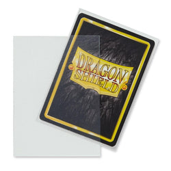 A clear, durable protective card sleeve is shown, featuring a playing card partially inserted into it. The card has a "Dragon Shield" logo with a yellow shield design and red text, set against a textured black background with a yellow border. The transparent sleeve clearly displays the card within. This product is Dragon Shield: Standard 100ct Sleeves - Clear (Matte) by Arcane Tinmen.