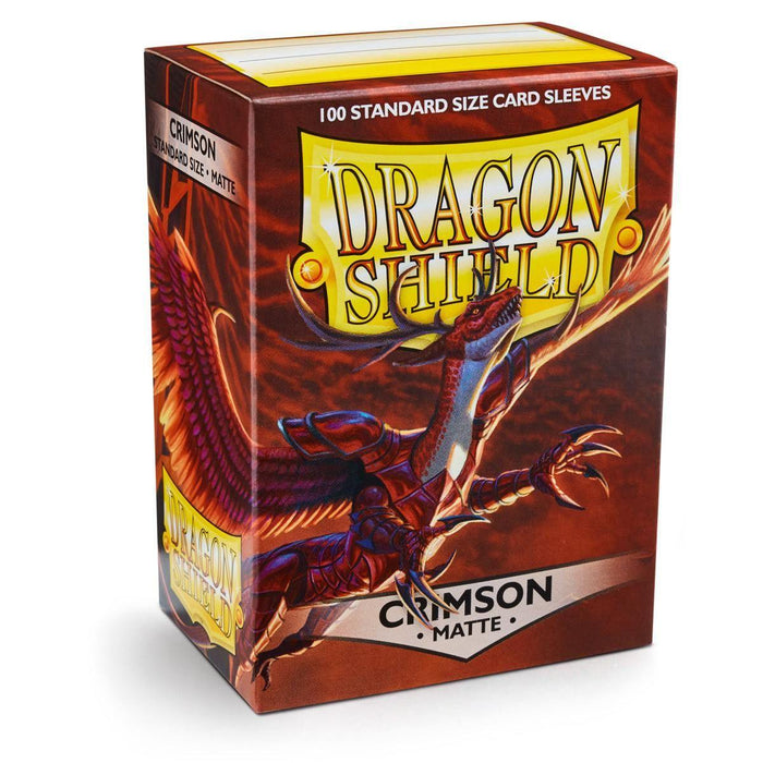 A box of Arcane Tinmen Dragon Shield: Standard 100ct Sleeves - Crimson (Matte) with "Crimson - Matte" written on it, containing 100 matte sleeves. The packaging features a detailed illustration of a fierce, red dragon with wings spread amidst a dynamic background of fiery colors. The Dragon Shield logo is prominently displayed in bold letters.