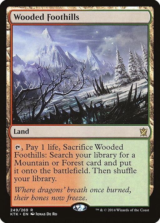 A Magic: The Gathering card titled "Wooded Foothills [Khans of Tarkir]." This Rare Land depicts a mountainous landscape with jagged peaks and frosty trees under a cloudy sky. The card text reads: Tap, pay 1 life, sacrifice Wooded Foothills [Khans of Tarkir]: Search your library for a Mountain or Forest card and put it onto the battlefield. Shuffle your library. Below, it states, Magic: The Gathering.