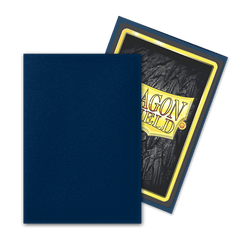 The image shows two Dragon Shield: Japanese Size 60ct Sleeves - Midnight Blue (Matte) by Arcane Tinmen. One sleeve is plain dark blue and is positioned in front of another sleeve that displays the back of a card featuring the "Dragon Shield" logo with a gold border, textured dark background, and yellow text. The card sleeves overlap slightly.