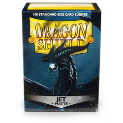 The image showcases a box of Arcane Tinmen's Dragon Shield: Standard 100ct Sleeves - Jet (Matte). The dark box features an illustration of a black dragon with blue accents. "Dragon Shield" is emblazoned in large, golden letters at the top, with "100 Standard Size Durable Card Sleeves" and "Jet Matte" below.