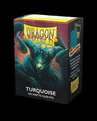 A box of Arcane Tinmen Dragon Shield: Standard 100ct Sleeves - Turquoise (Matte) is shown, featuring an illustration of a turquoise dragon with sharp horns and wings, emitting a fierce aura. Designed in turquoise and blue hues, the box contains 100 trading card sleeves. The bottom label reads "TURQUOISE 100 MATTE SLEEVES.