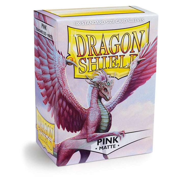 The image displays a box of Dragon Shield: Standard 100ct Sleeves - Pink (Matte) by Arcane Tinmen, adorned with an image of a pink dragon with large wings against a cloudy background. The text reads "Dragon Shield" in large, yellow letters and "100 Standard Size Card Sleeves" at the top, with "Pink Matte" at the bottom.