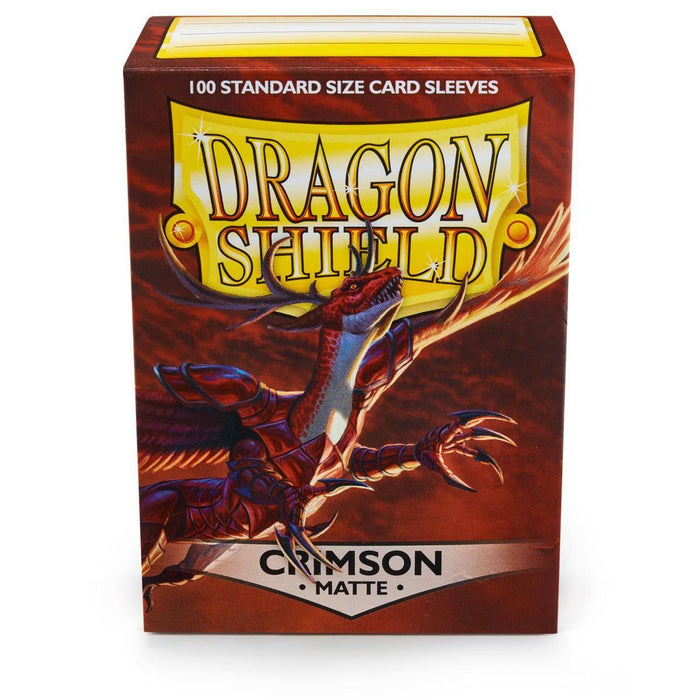 A box of Dragon Shield: Standard 100ct Sleeves - Crimson (Matte) by Arcane Tinmen, designed in crimson. The box features an illustration of a fierce red dragon with wings spread and claws extended. The text at the top reads "100 Standard Size Card Sleeves" and "Dragon Shield" in a bold, yellow font with a shield graphic.