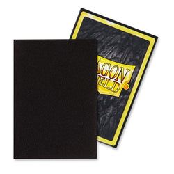 Two card sleeves are displayed. One is plain black, covering most of the other sleeve, which is partially visible behind it. The visible Japanese size sleeve has a colorful design with the words "Dragon Shield" in large, stylized yellow and red font, bordered by a bright yellow and black frame. The product displayed is Arcane Tinmen’s Dragon Shield: Japanese Size 60ct Sleeves - Black (Matte).