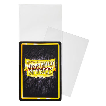 The image shows a pack of Arcane Tinmen's Dragon Shield Japanese Size 100ct Inner Sleeves - Perfect Fit (Clear 'Qyonshi'). One transparent sleeve slightly open reveals a card with a textured black background and bright yellow border featuring the Dragon Shield logo, while another sleeve lies flat behind.