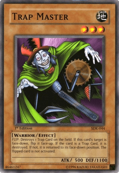 Image of the Yu-Gi-Oh! Effect Monster "Trap Master [SDK-044] Common" from Starter Deck: Kaiba. The card features an eerie character with a green cloak, a jester-like hat, and a sinister grin, wielding a saw blade. It's labeled Earth attribute, Warrior/Effect type, ATK 500, DEF 1100, with text explaining its effects. Card identifier: SDK