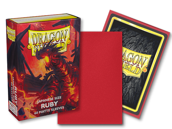 The image showcases a Dragon Shield: Japanese Size 60ct Sleeves - Ruby (Matte) box from Arcane Tinmen, featuring artwork of a red dragon on the cover. The text "Japanese Size Ruby - 60 Matte Sleeves" is clearly visible. Beside the box, there's a red card sleeve, and behind it is a card with the Dragon Shield logo on a black, textured background—making these ideal TCG sleeves for collectors.